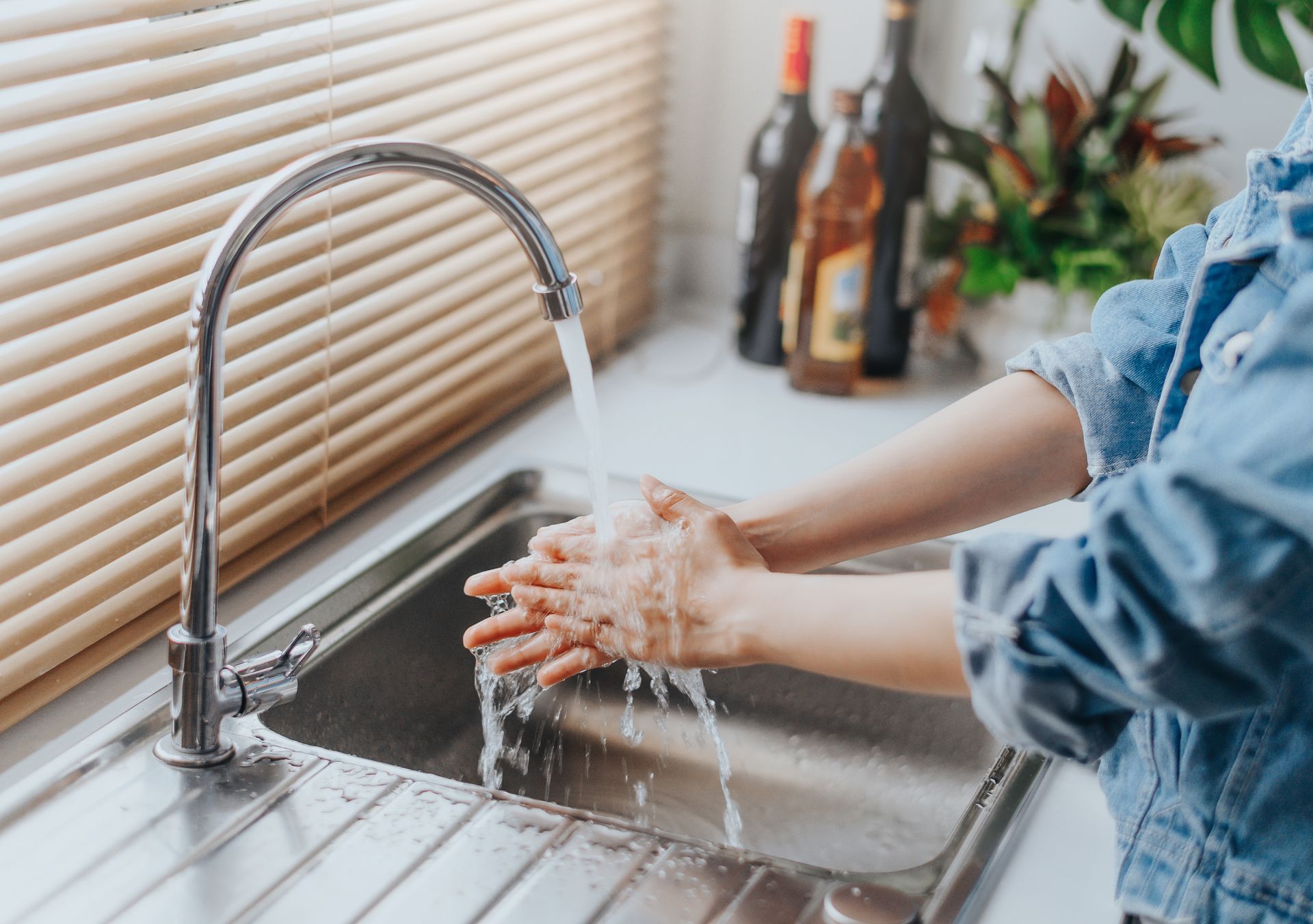 A woman is washing her hands in a kitchen sink.