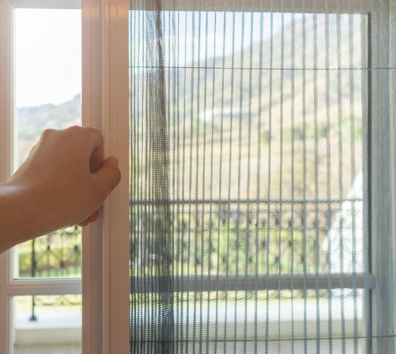 Person installing a black framed window screen against a white wall.