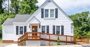 White house with brown ramp and shutters, set in front of trees.