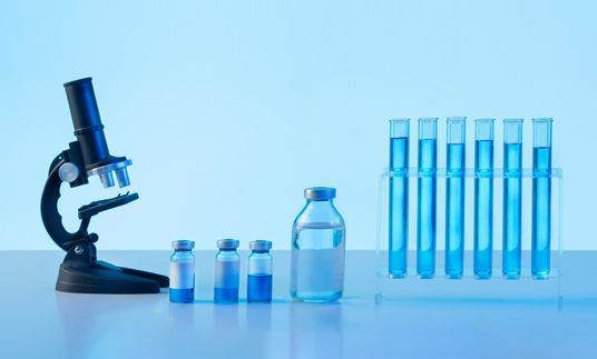 Un microscope, des tubes à essai et des bouteilles de liquide bleu sur une table.
