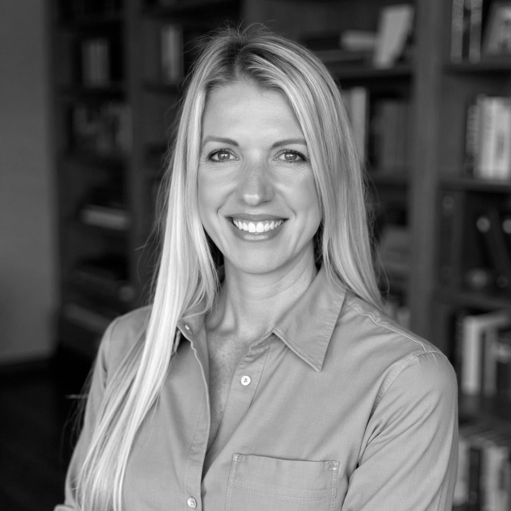 Sarah Whatley in a button-up shirt in a blurred bookshelf-lined office