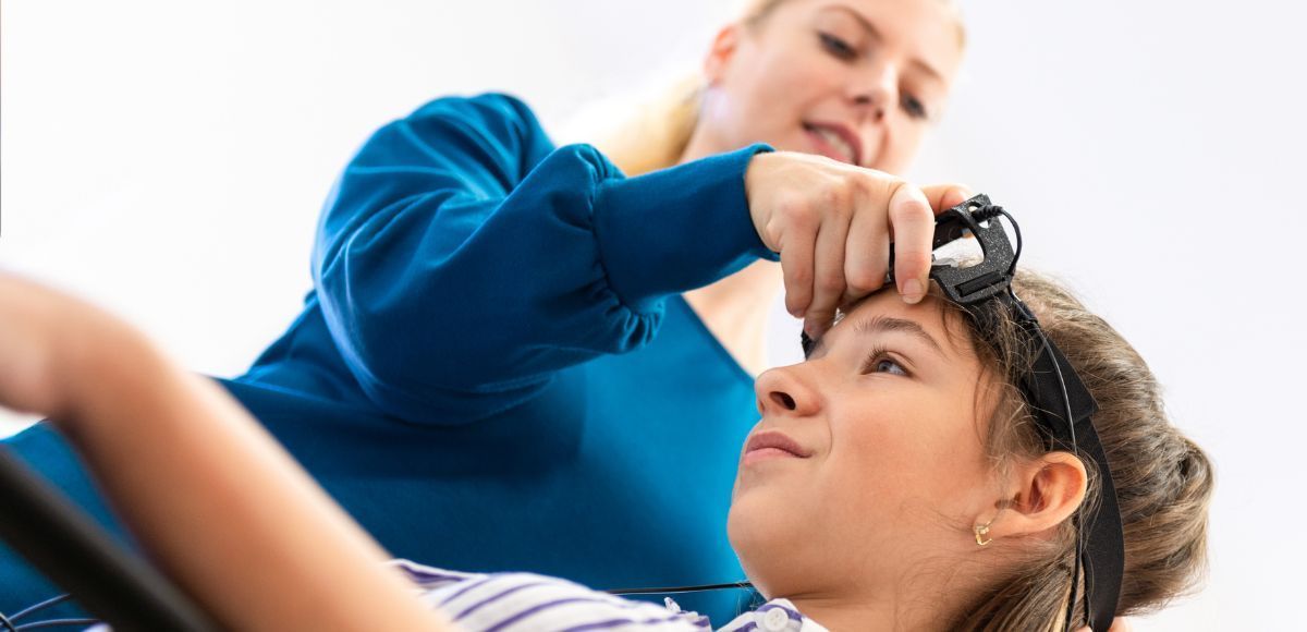 A calm clinical setting showing a person seated with neurofeedback sensors on their scalp, looking r