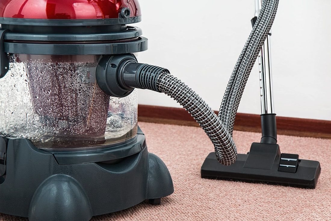 Red and black vacuum cleaner with clear dust container on a pink carpet.