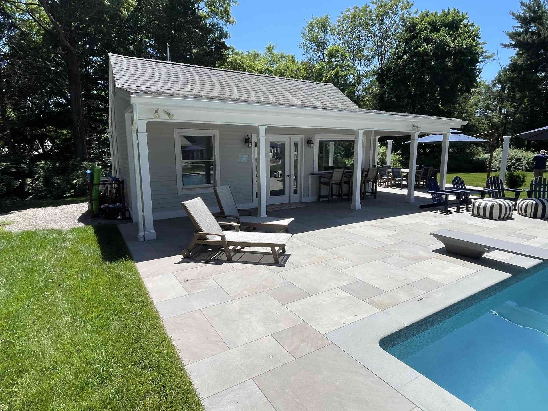 White pool house with patio loungers beside a blue swimming pool on a sunny day