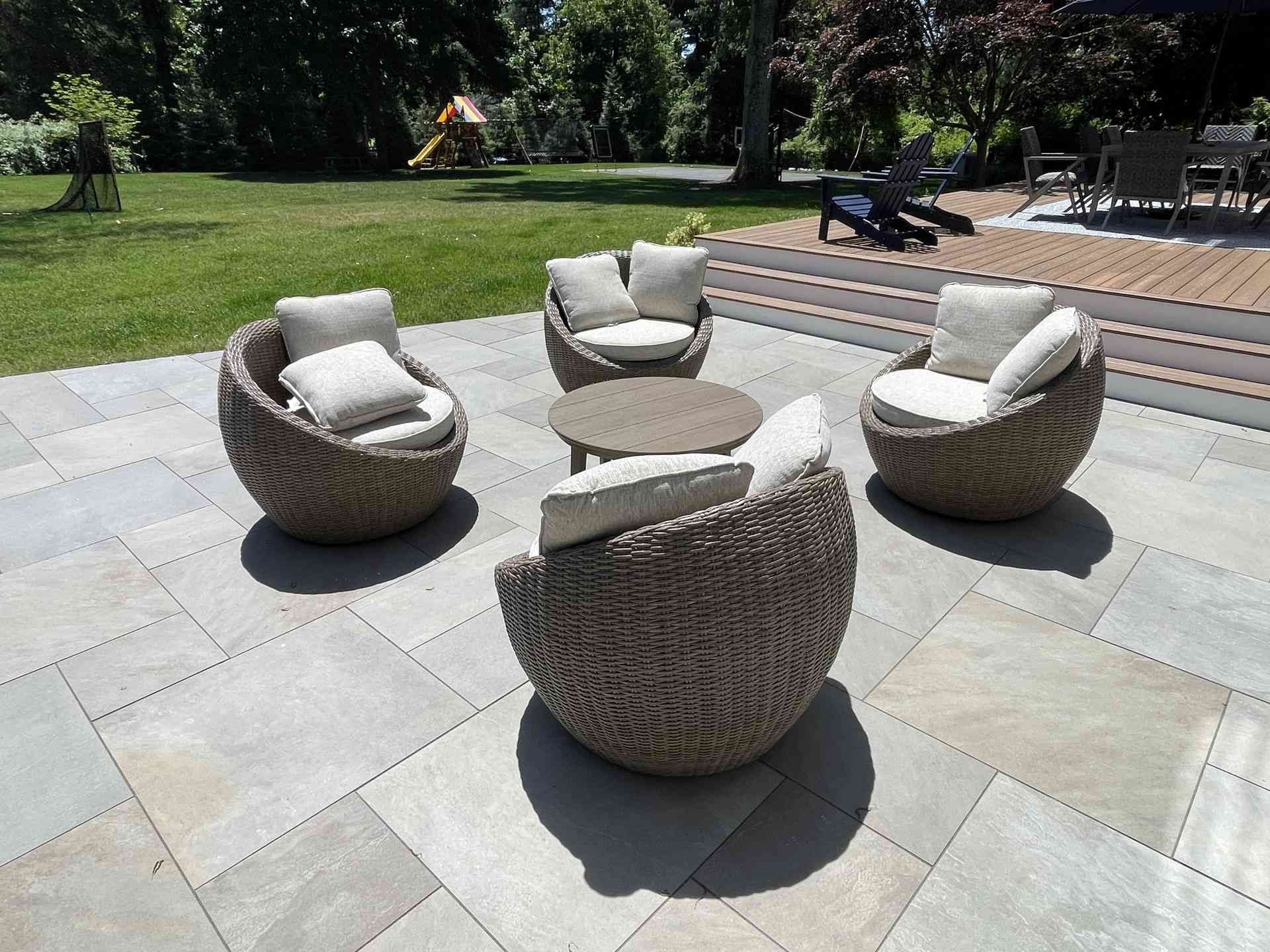 Round wicker patio chairs with white cushions on a stone terrace in a sunny garden