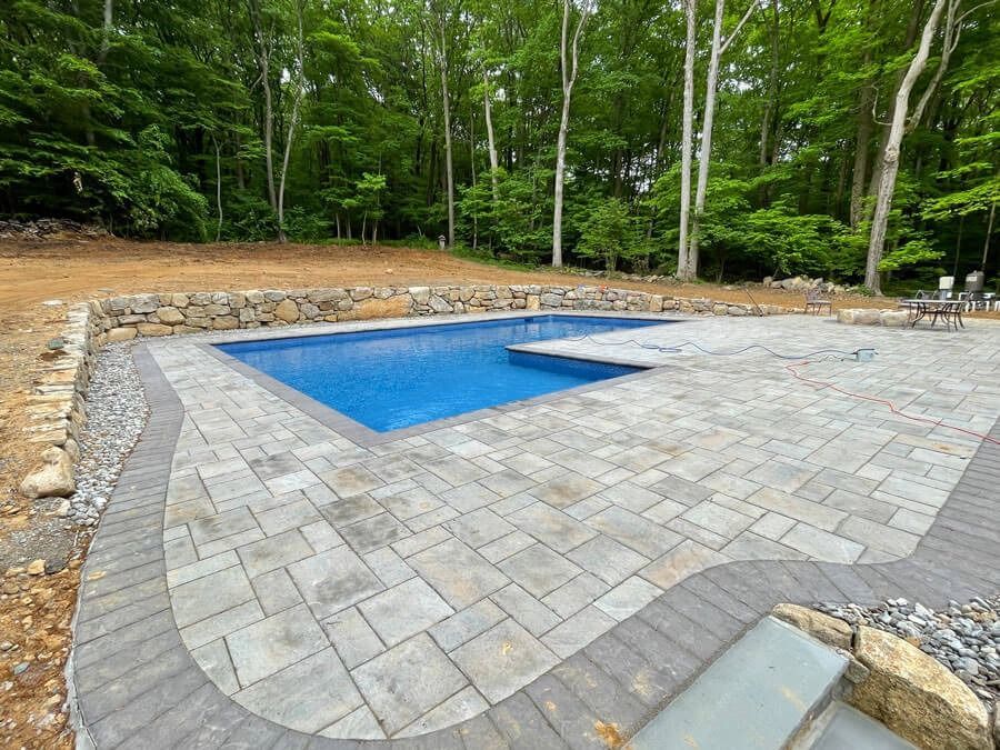 Backyard patio with a small blue swimming pool surrounded by stone pavers and trees