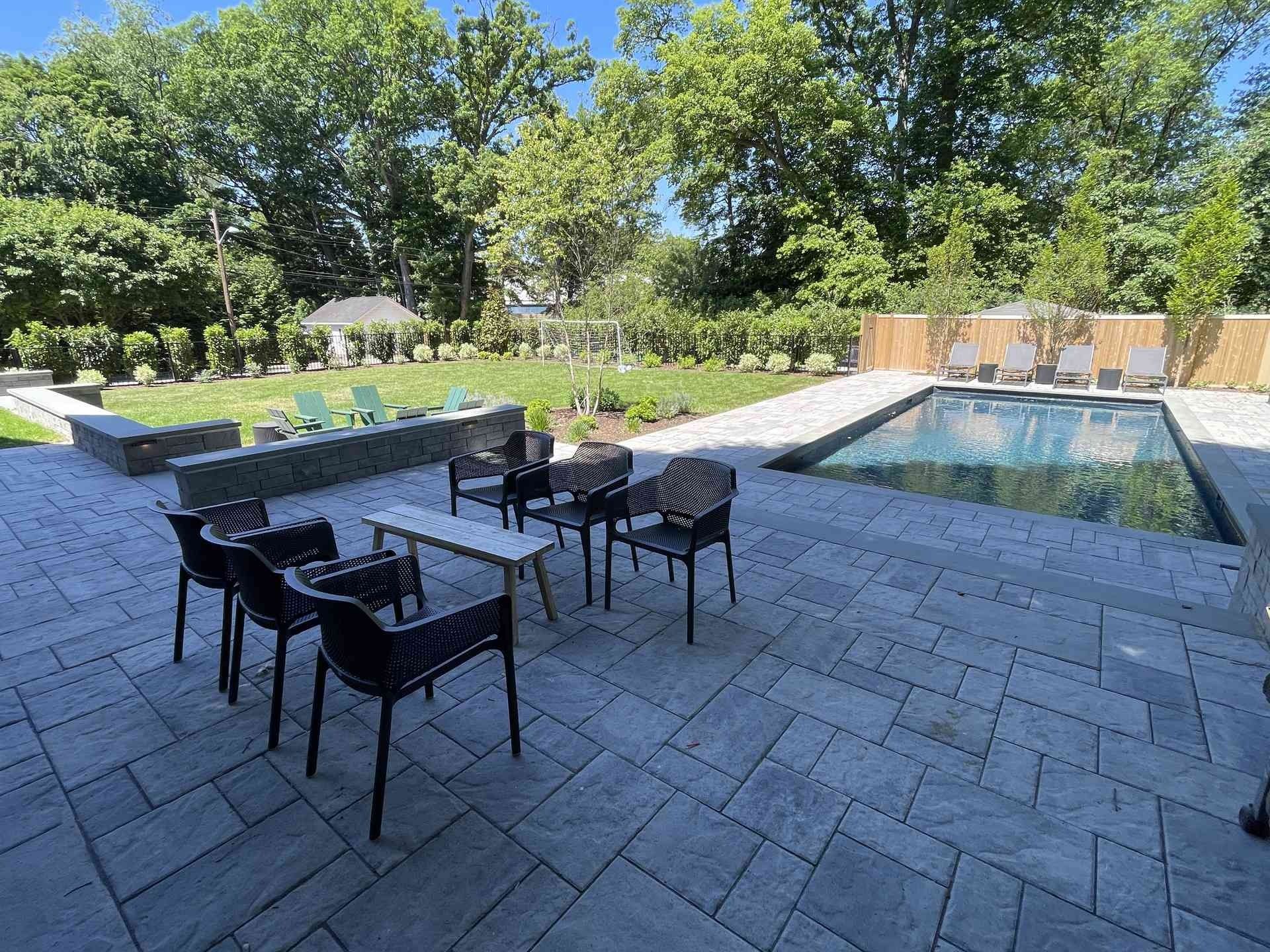 Patio seating beside a rectangular pool and garden with trees in the background