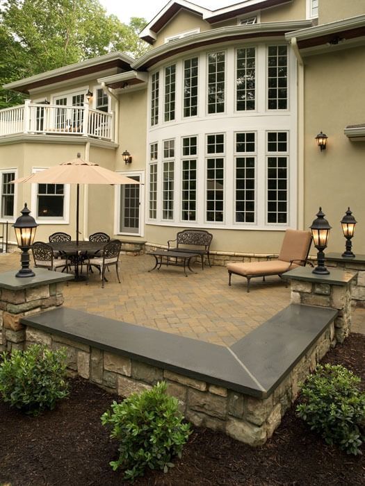 Stone patio with outdoor seating and large white bay windows on a beige house