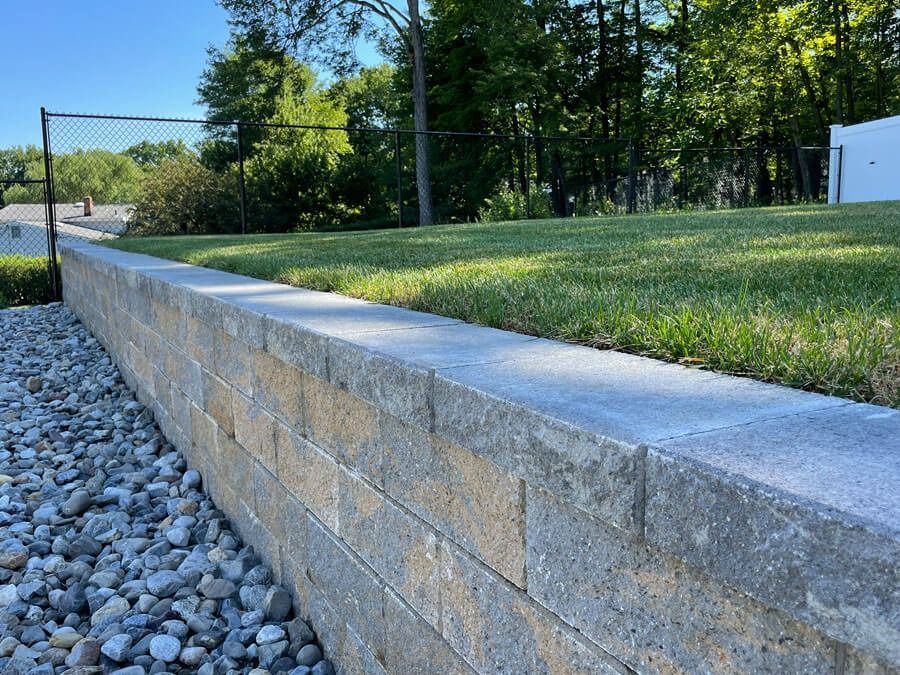 Concrete retaining wall beside a gravel path and grassy yard under trees