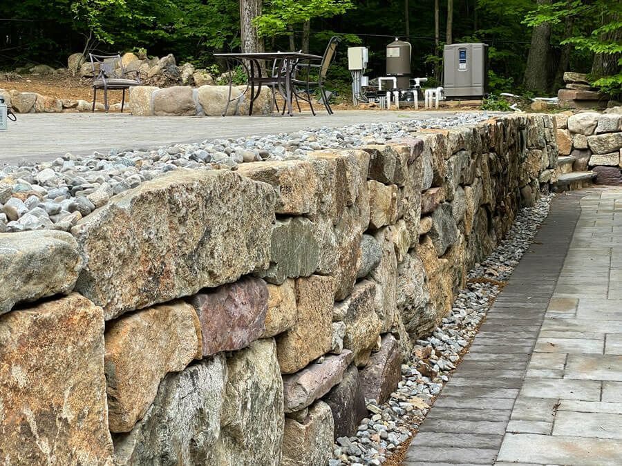Stone retaining wall beside a paved patio in a landscaped outdoor area
