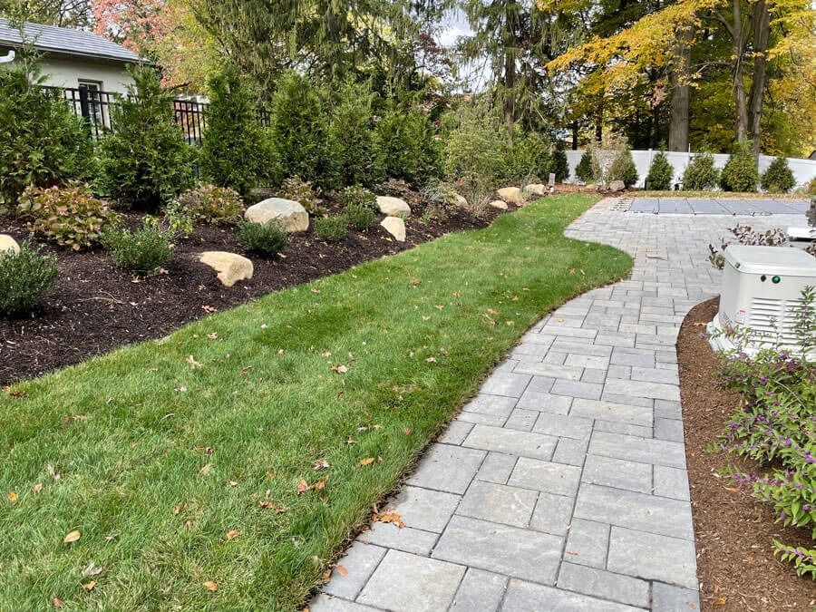 Curved stone walkway beside a manicured lawn and landscaped garden beds with shrubs and flowers