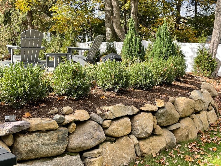 Stone retaining wall with shrubs and Adirondack chairs in a landscaped garden