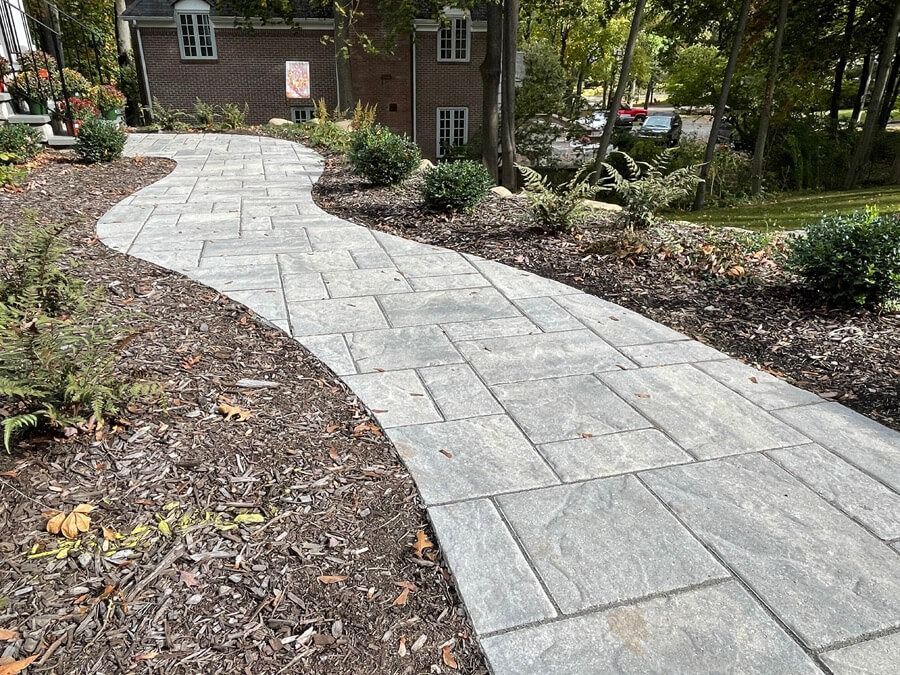 Curved stone walkway through a landscaped garden toward a brick building entrance