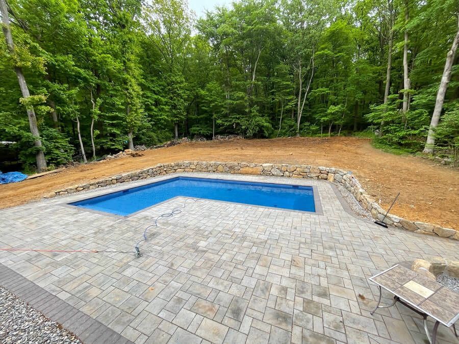 Backyard patio with a covered rectangular pool and stone pavers, surrounded by trees
