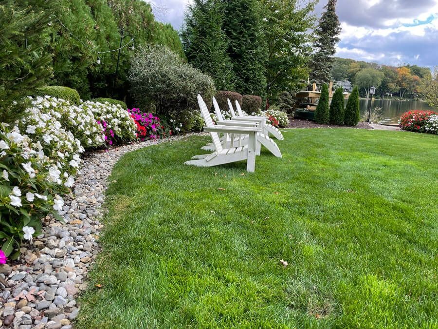 White Adirondack chairs on a lush green lawn beside a colorful flower-lined garden path