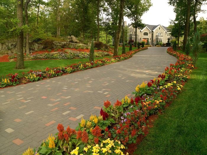 Curved garden pathway lined with colorful flower beds leading to a house