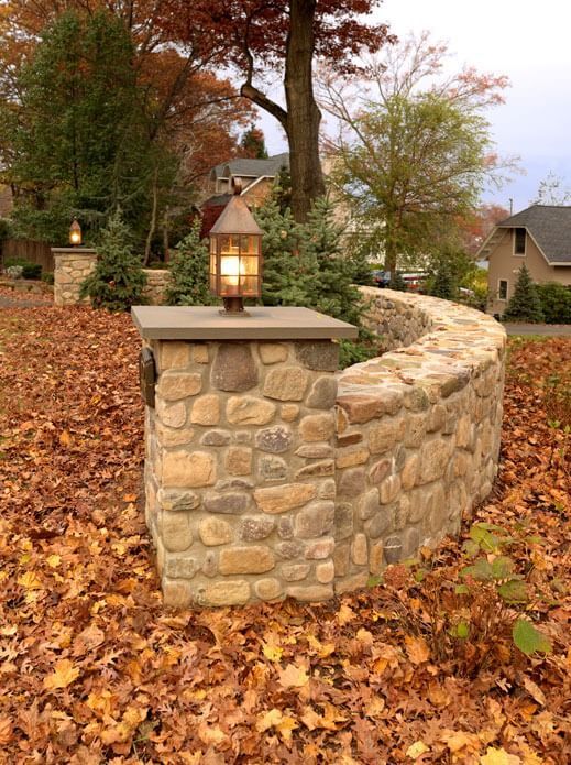 Stone garden wall with lantern beside a leaf-covered path in autumn