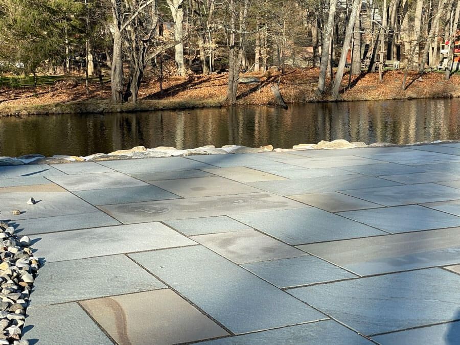 Stone patio by a calm pond with bare trees along the far shore.