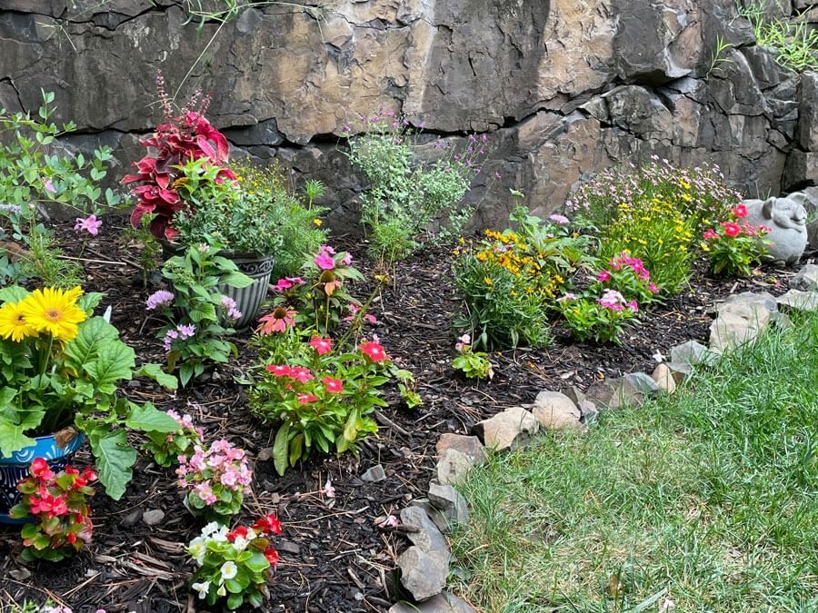 Colorful flower bed along a stone wall beside a grassy lawn