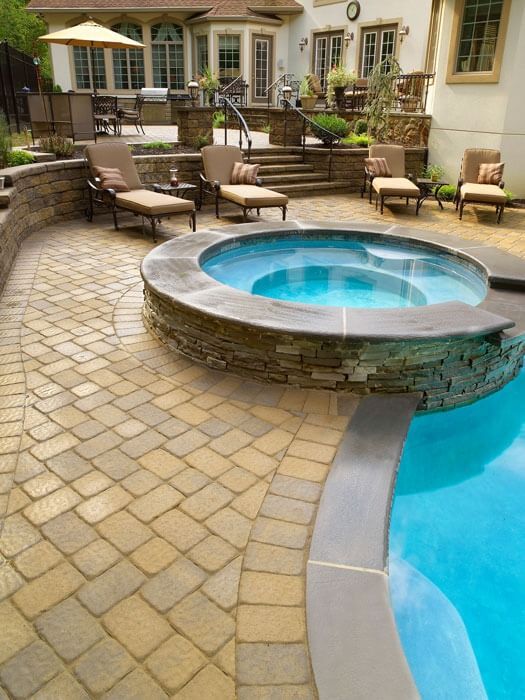 Stone patio pool area with a raised round spa beside a blue swimming pool and outdoor lounge chairs