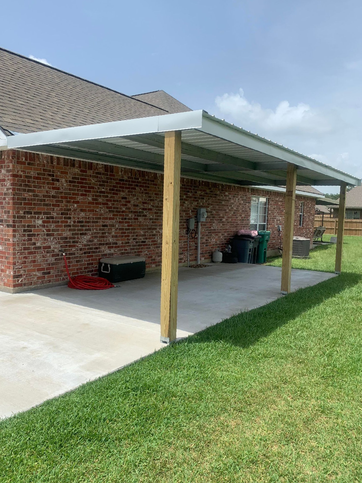 A carport with a white roof and wooden posts in front of a brick house.