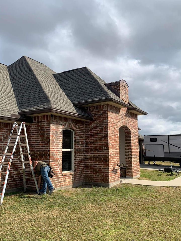 A man is standing on a ladder in front of a brick house.