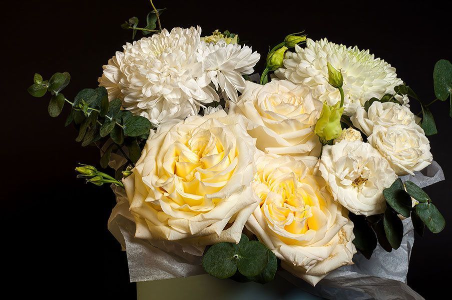 A bouquet of cream-colored roses and ruffled white carnations with green eucalyptus leaves against a black background.