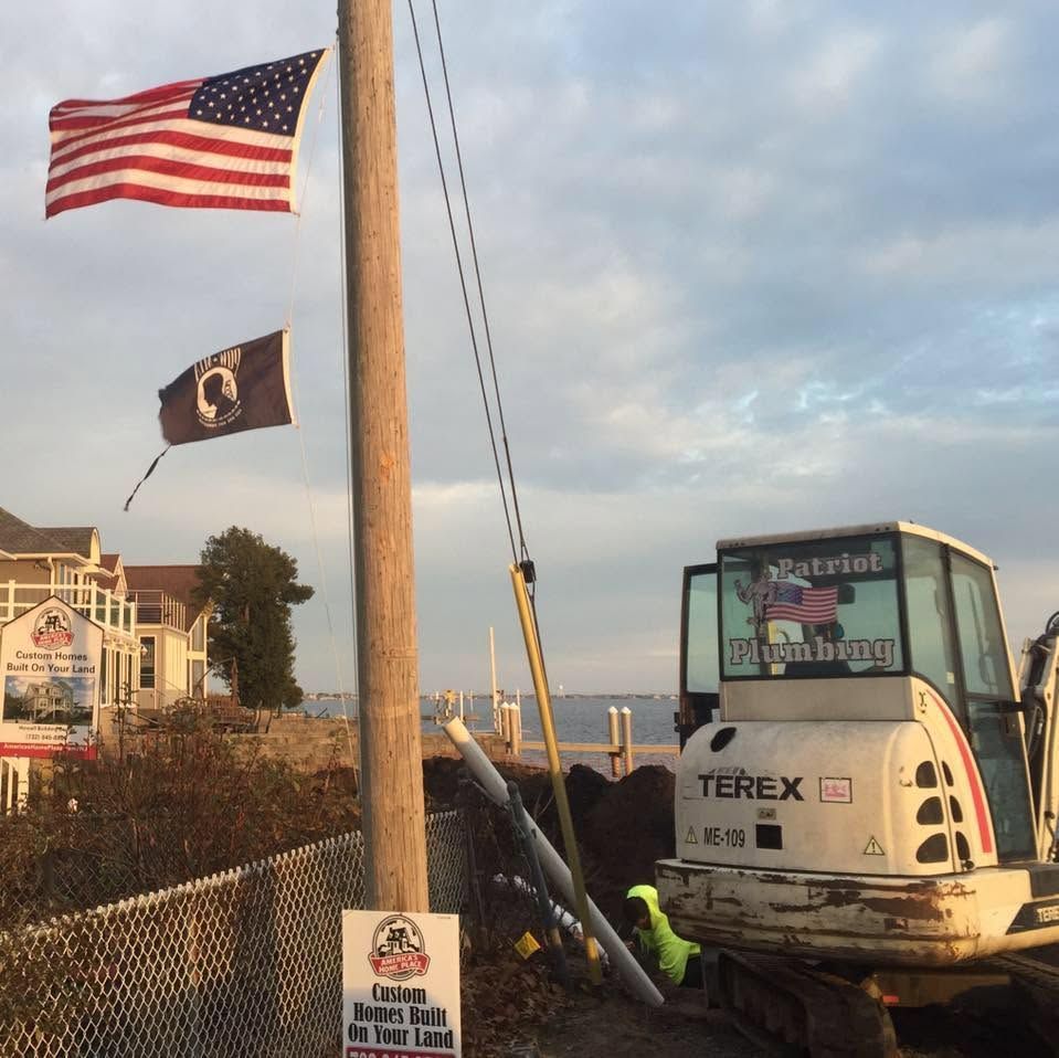 American and POW/MIA flags beside a Terex excavator on a roadside construction site at sunset