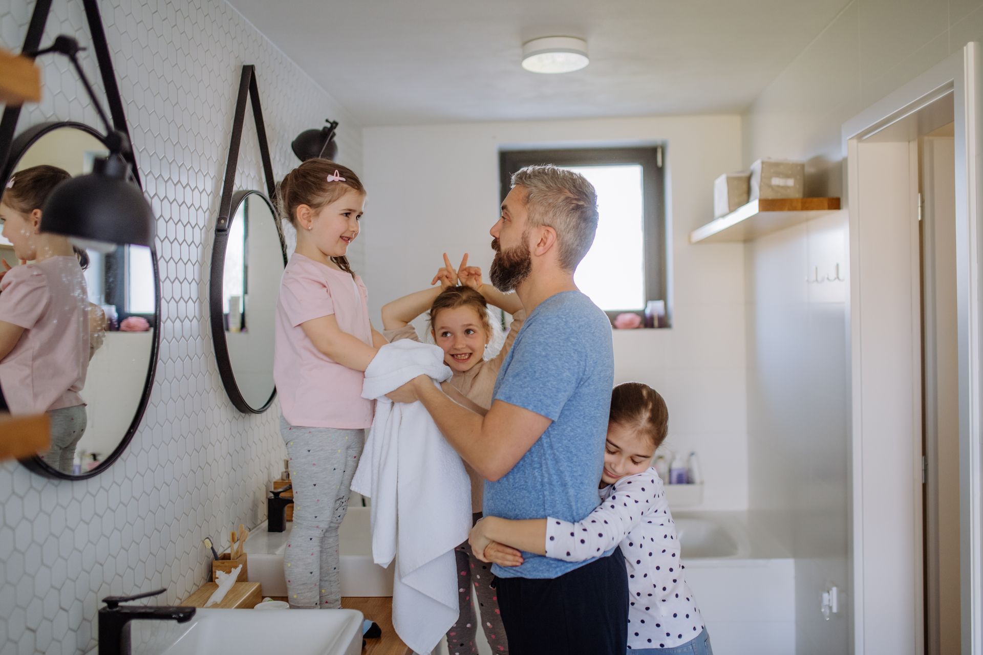 Parent holding children in a bright bathroom while another child hugs from the side