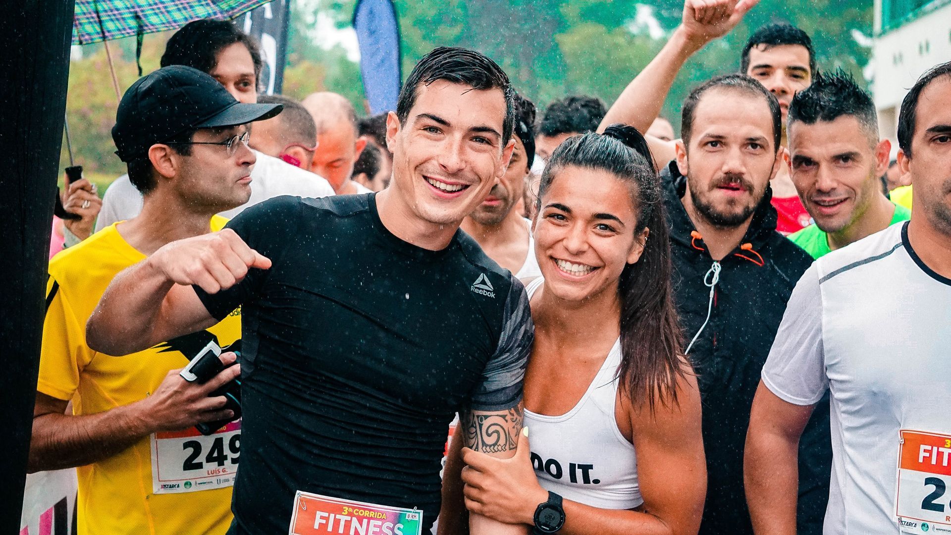 Runners smiling at a race start, wearing bibs and athletic shirts in a crowd