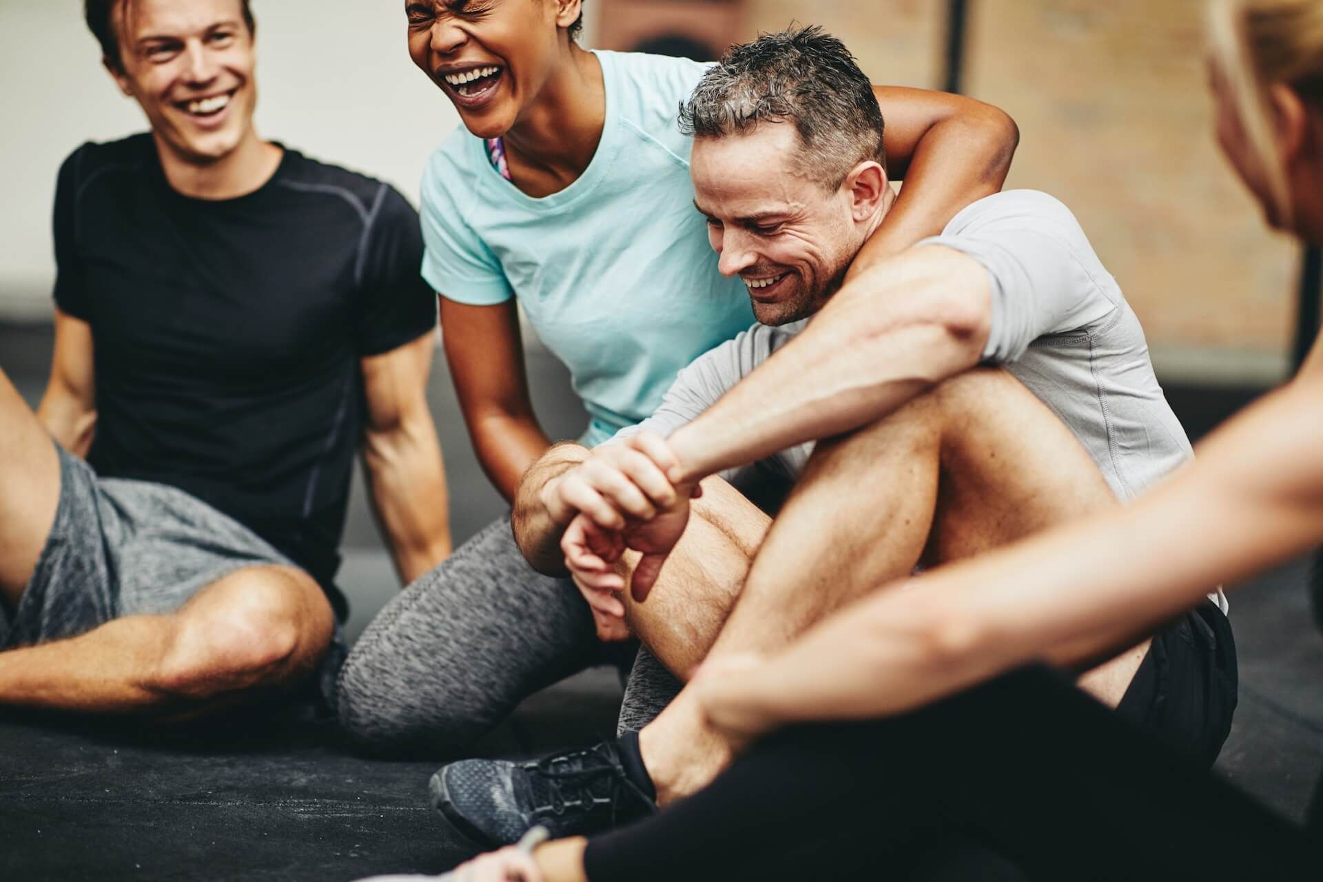Three smiling people sitting on a gym floor, chatting and relaxing after a workout