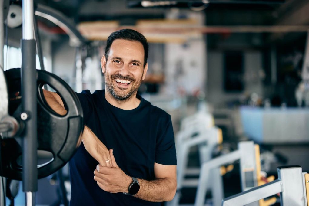 Smiling man in a black shirt leaning on gym equipment in a fitness center