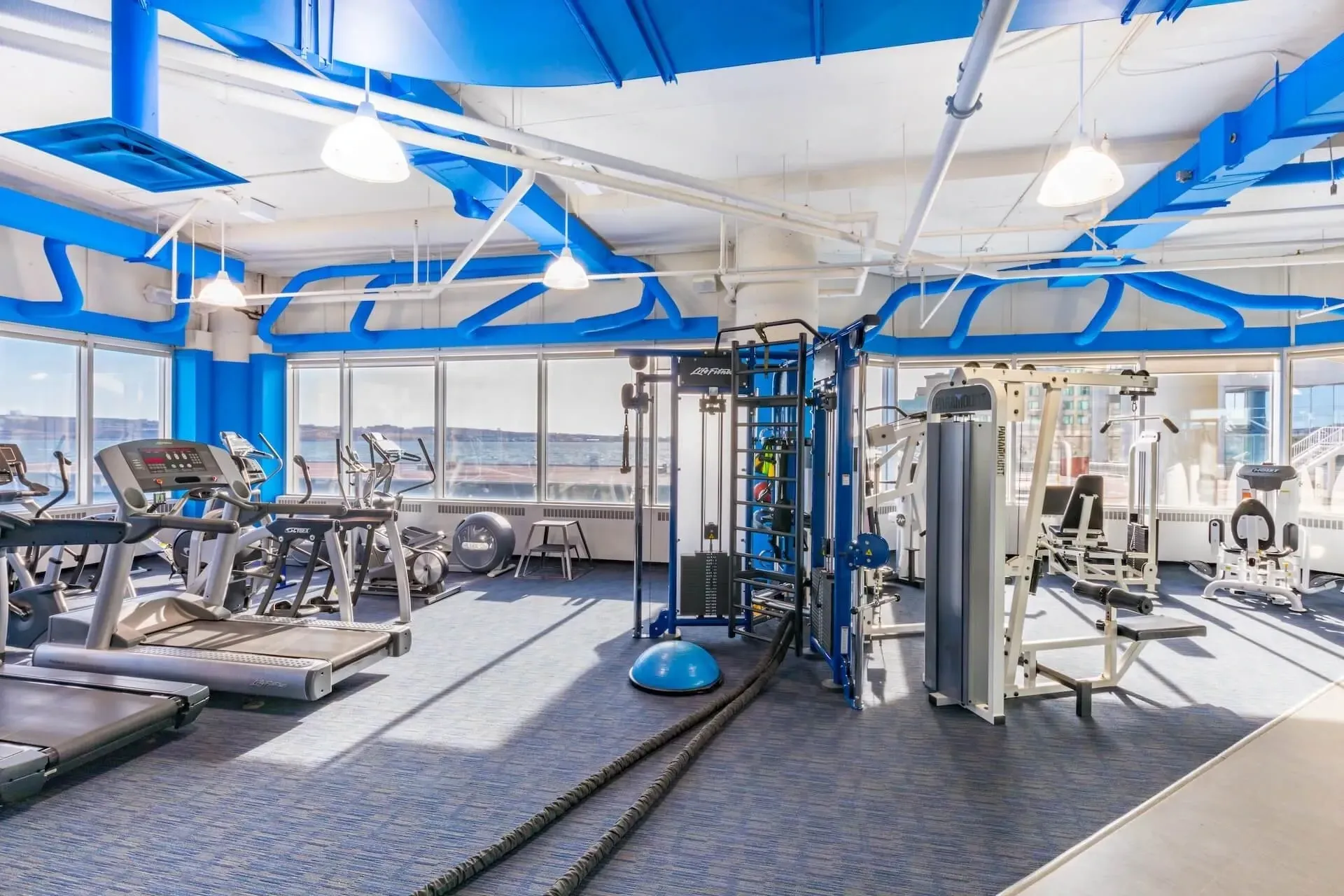 Bright modern gym with exercise machines, cable equipment, and blue-accented ceiling beams