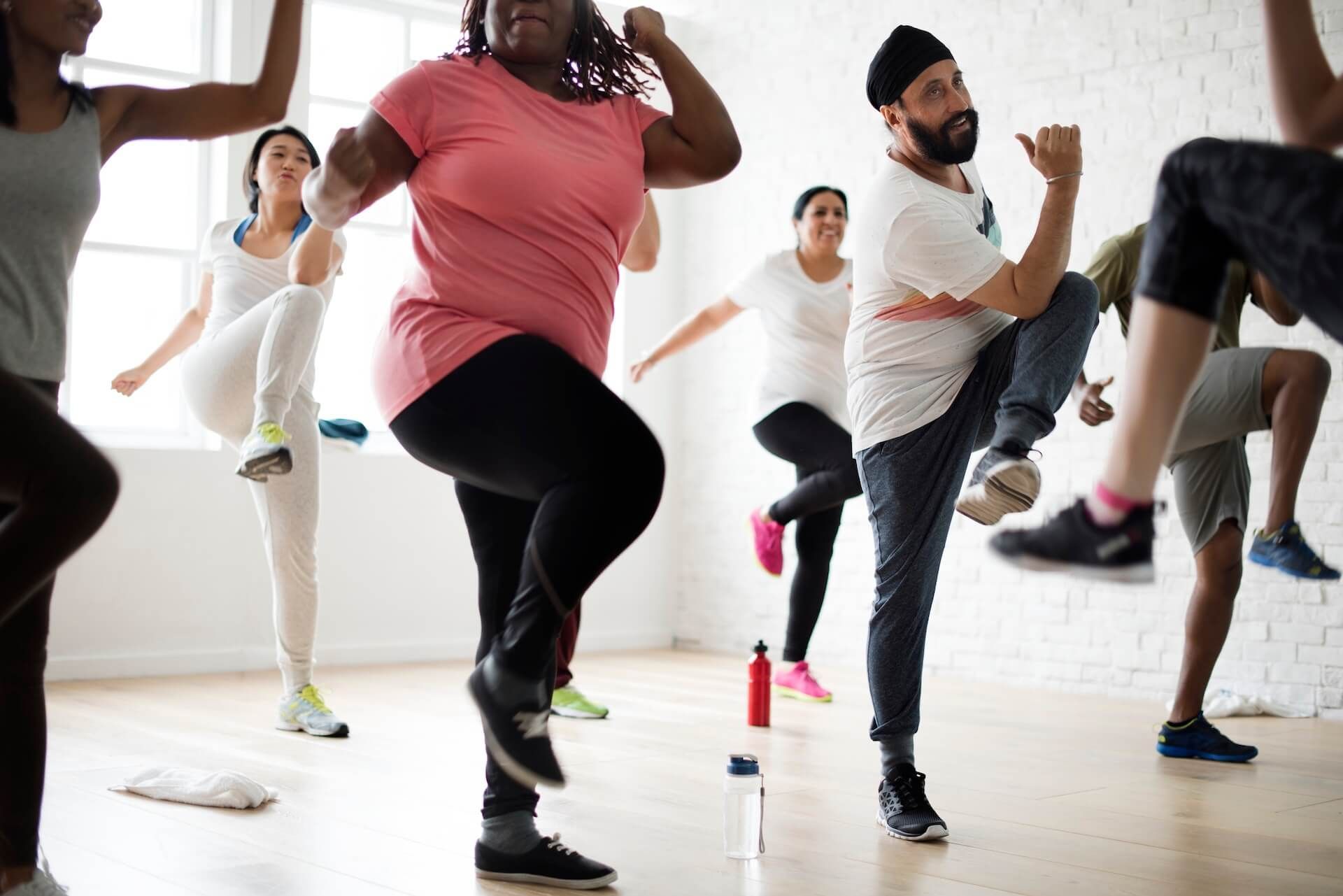 People doing a lively fitness dance class in a bright studio, lifting knees and arms.