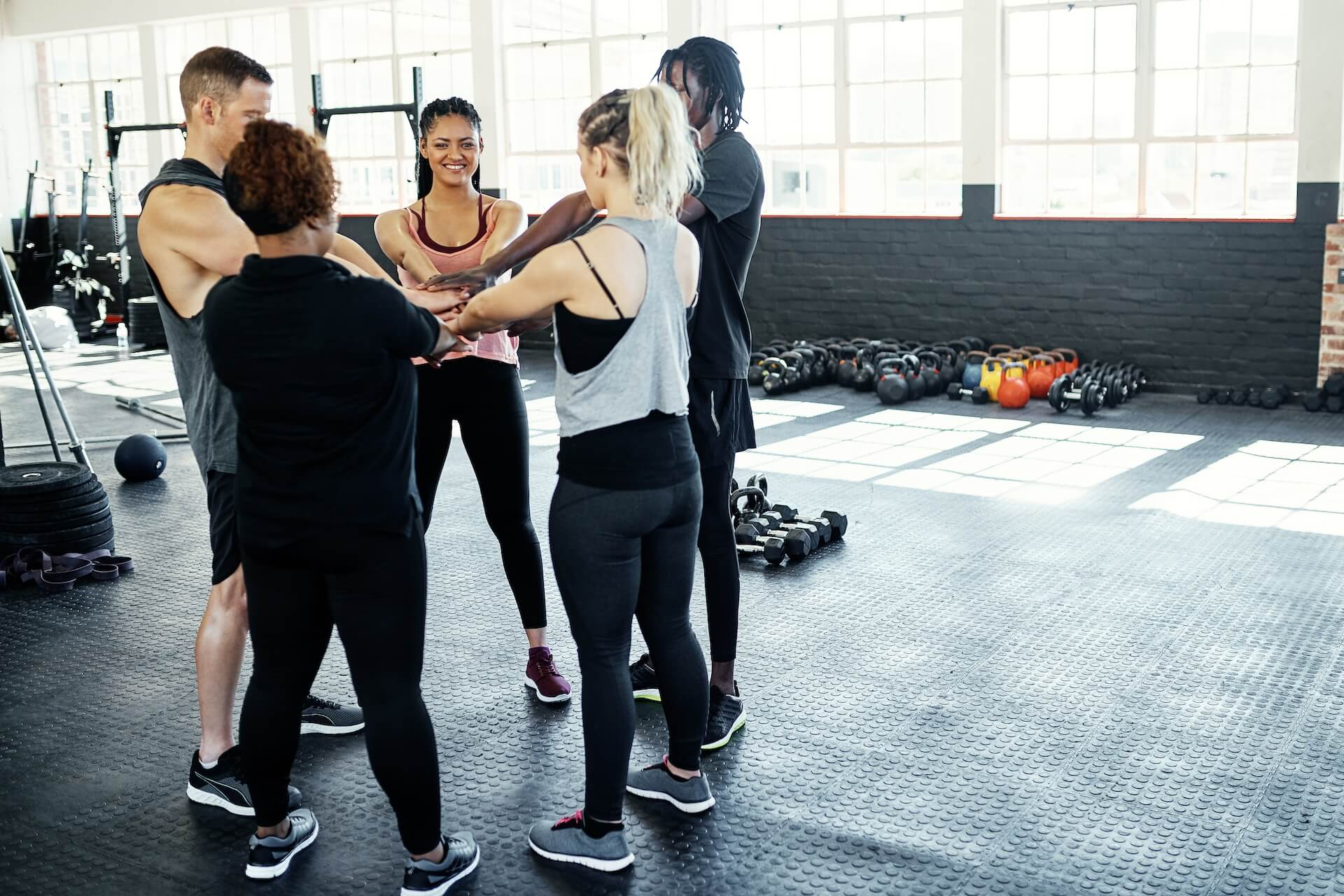 Fitness class standing in a circle in a bright gym, talking before exercise.