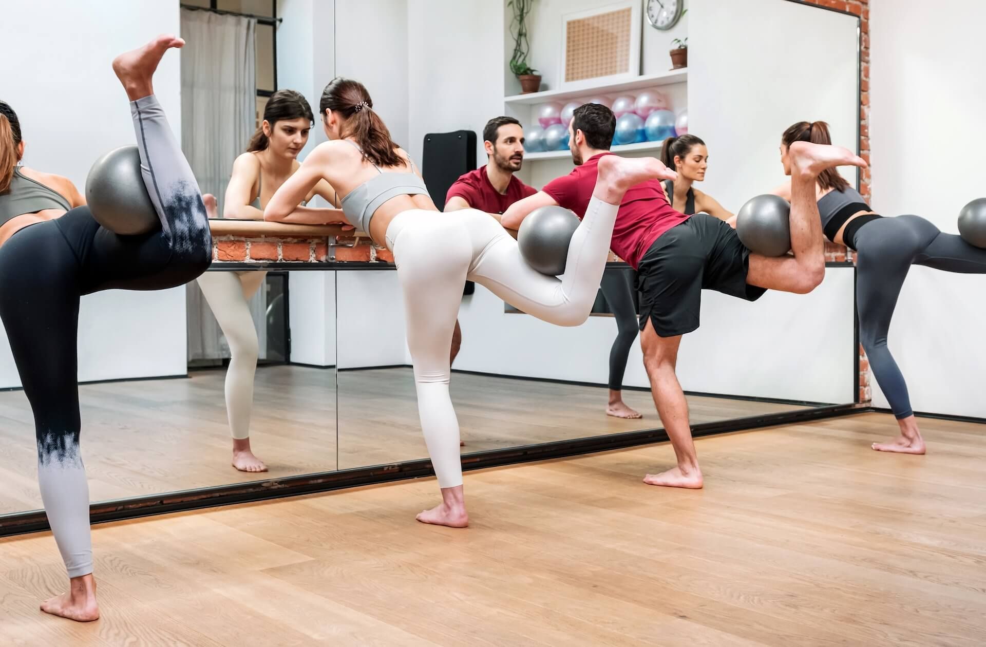 People practicing a dance or fitness class with mirrors in a bright studio, legs lifted in sync