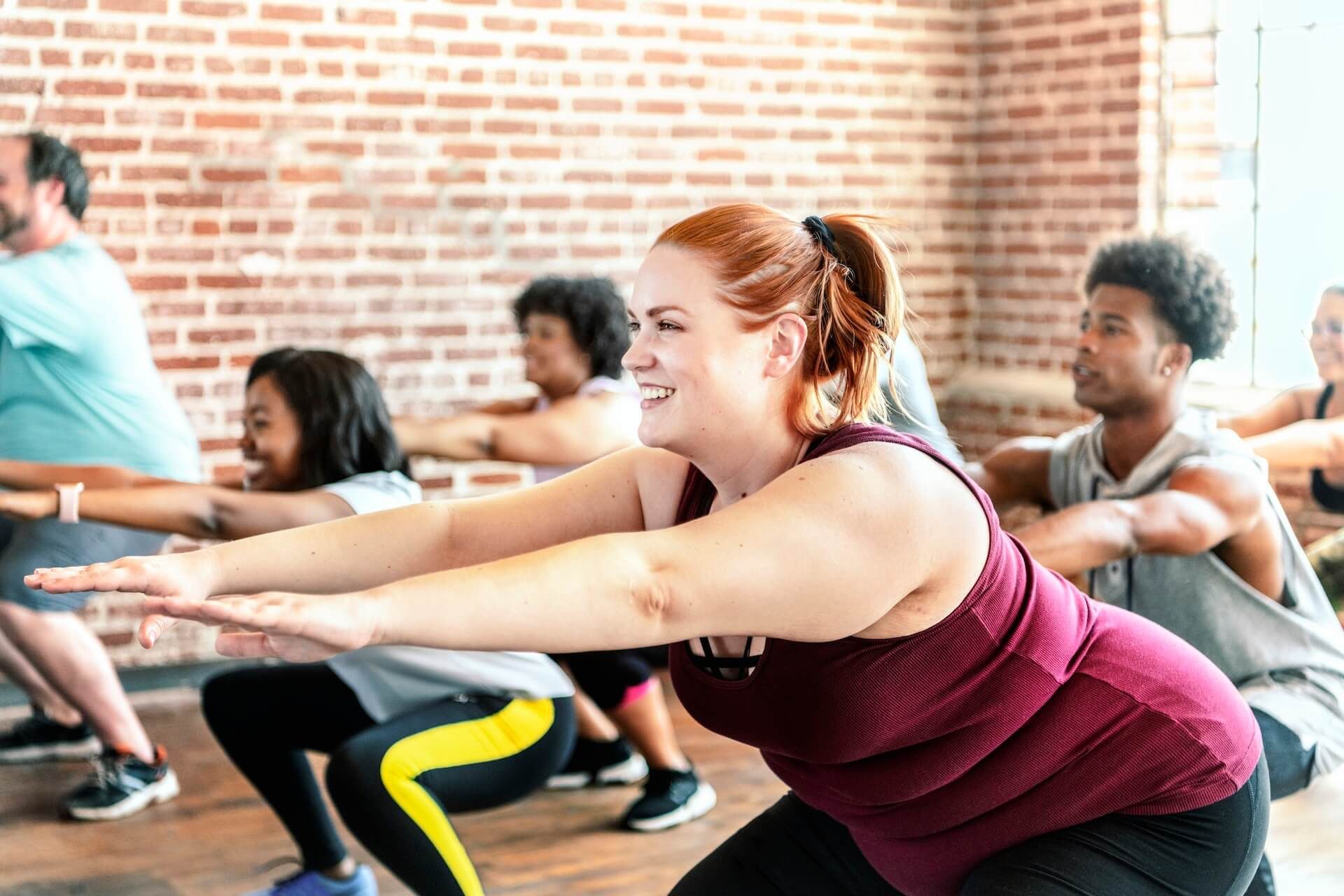 People doing squats in a bright fitness studio with a brick wall backdrop