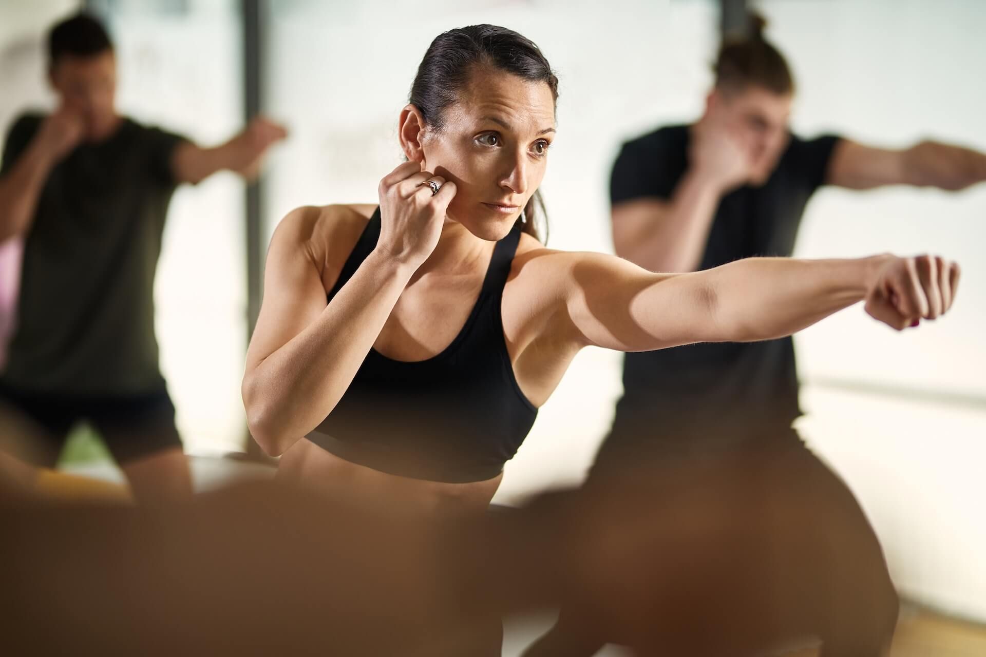 Group fitness class with a focused woman punching forward in a gym studio