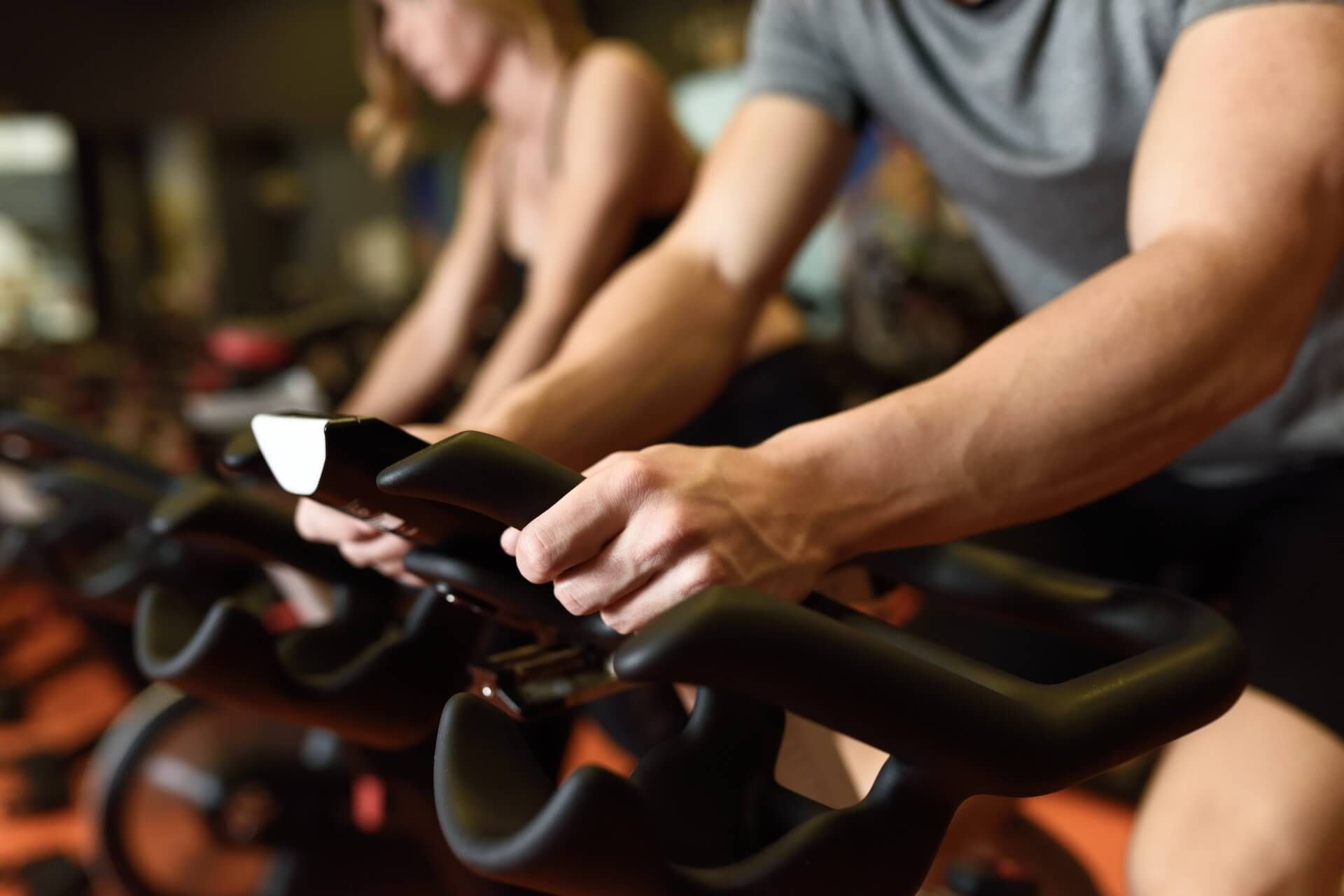 People pedaling stationary bikes in a gym class, hands on handlebars.