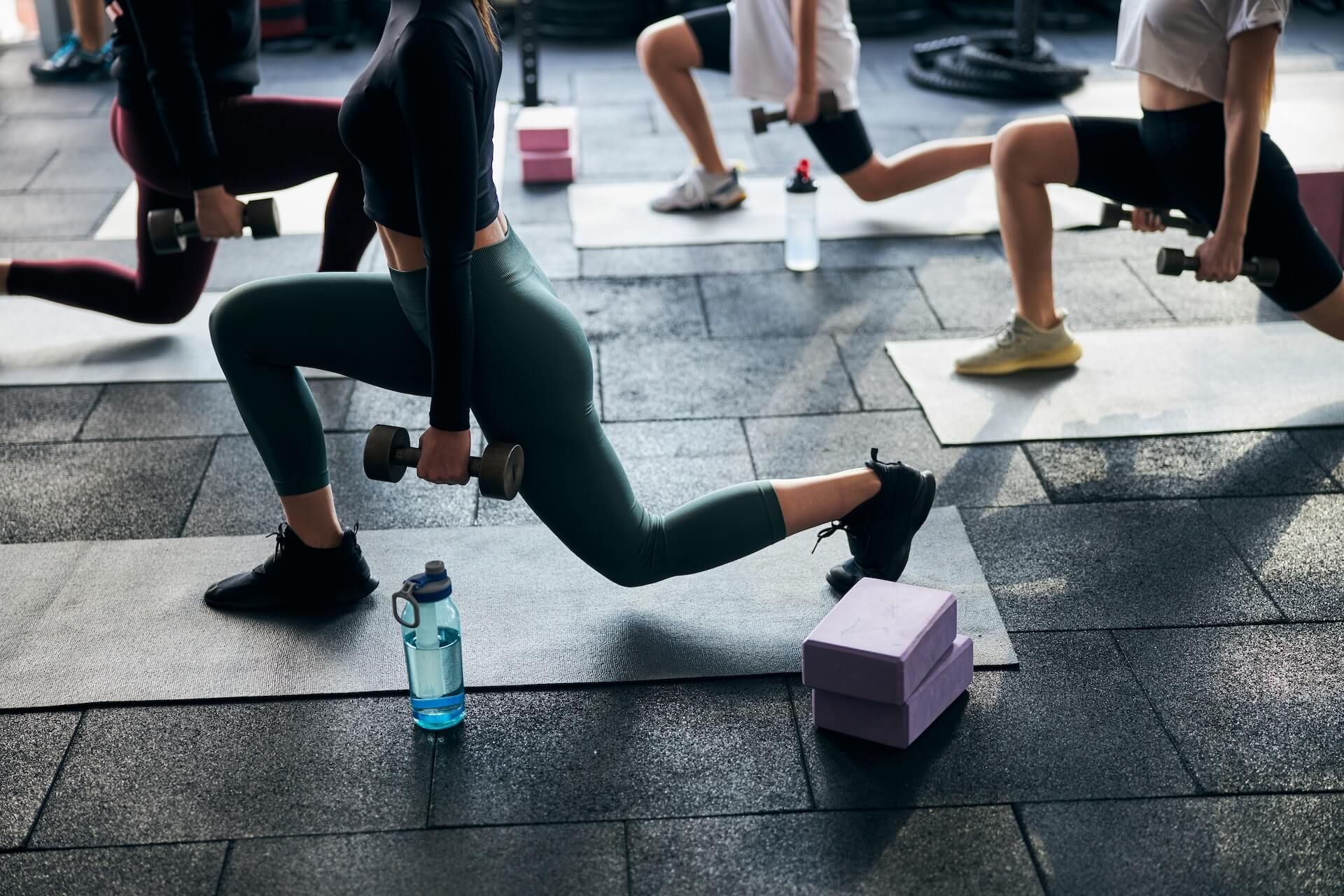 People doing a group lunge workout on a gym floor with water bottles and yoga blocks nearby
