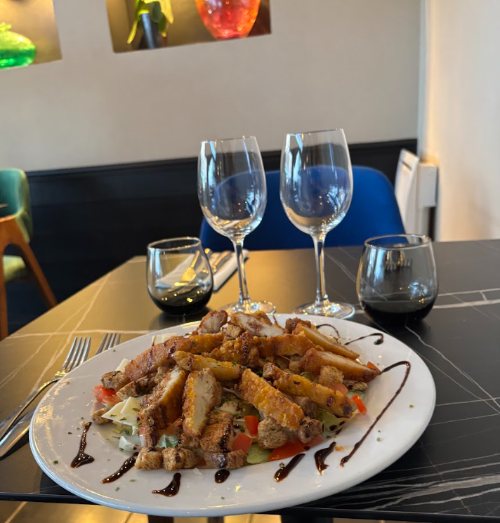 Jarret d'agneau avec sauce et frites, servi sur une assiette noire.