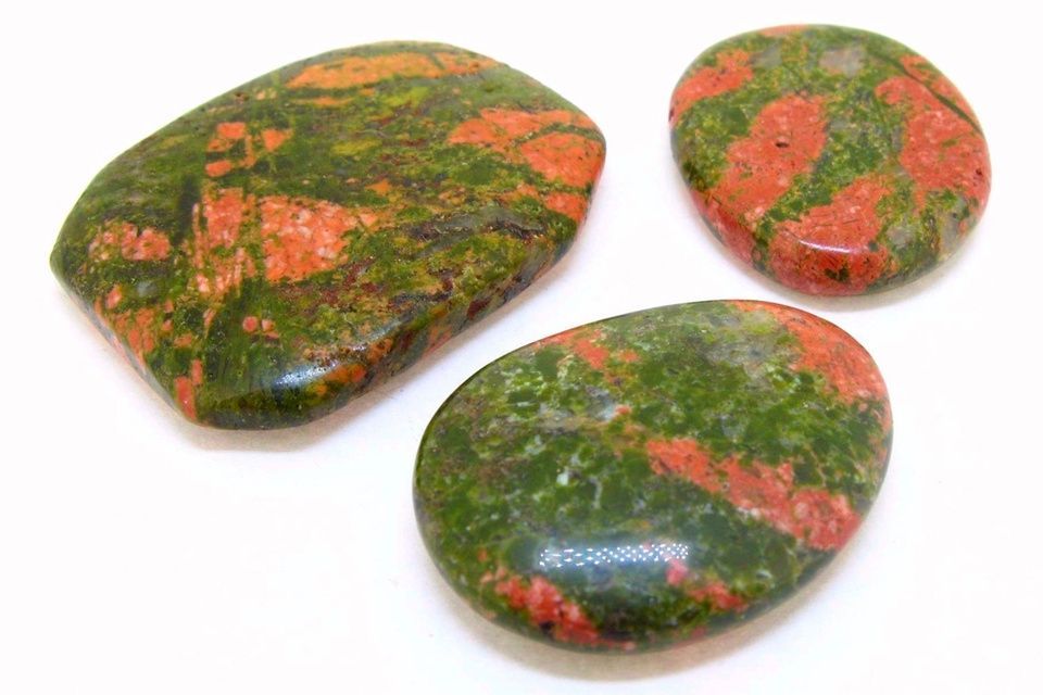 Tres piedras verdes pulidas con vetas rosadas y anaranjadas sobre un fondo blanco.