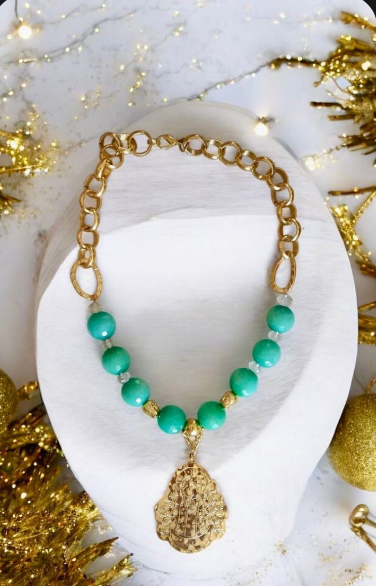 Collar de cuentas de oro y turquesa con un colgante en forma de lágrima sobre un busto blanco.