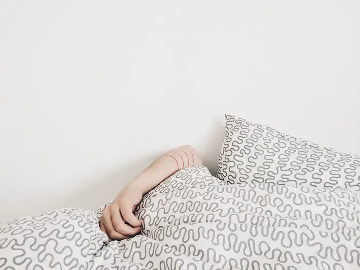 A person is under bed covers with only their arm hanging out and visible to see