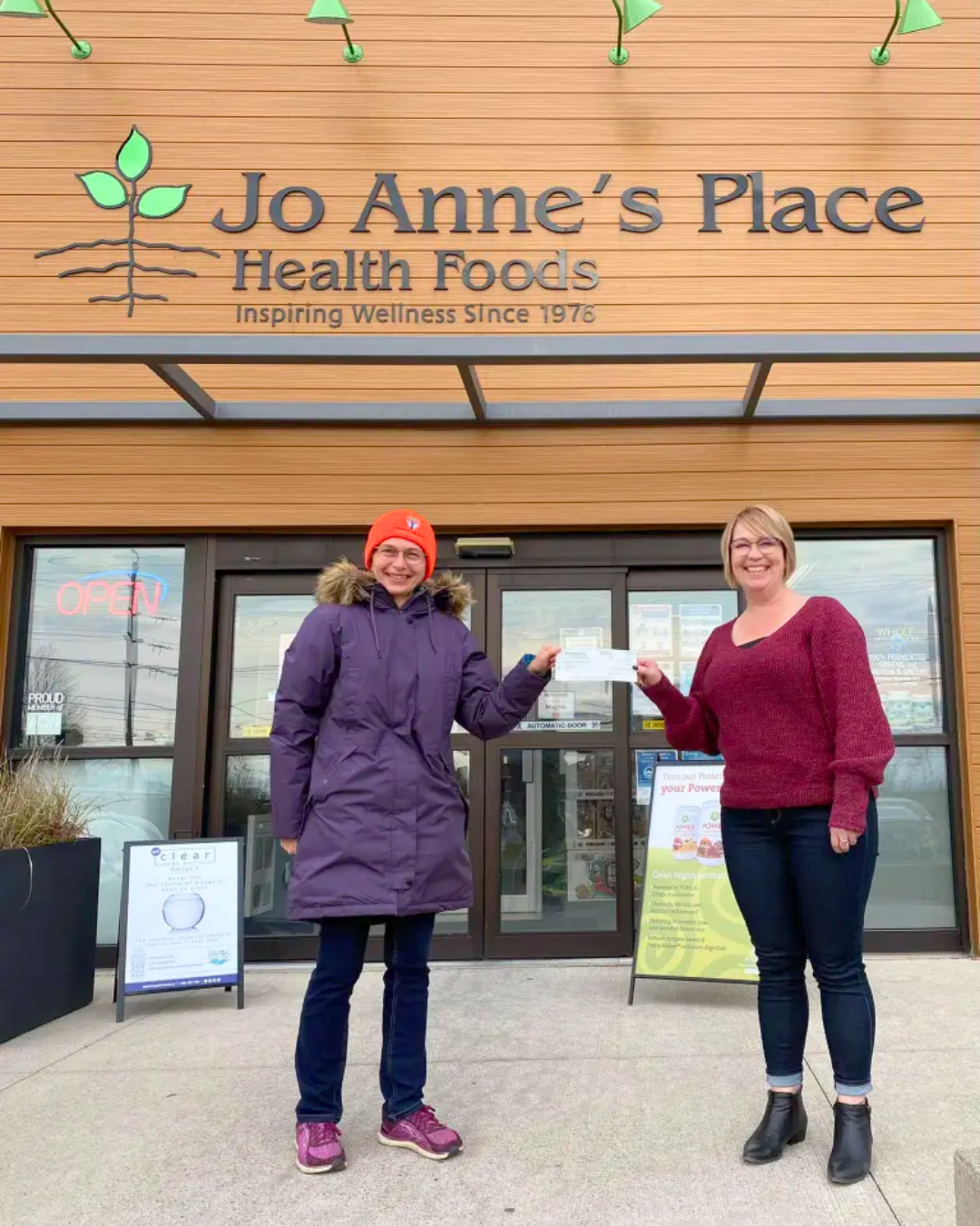 Two people stand outside the entrance to Jo Anne's Place Health Foods in Peterborough, holding a sign