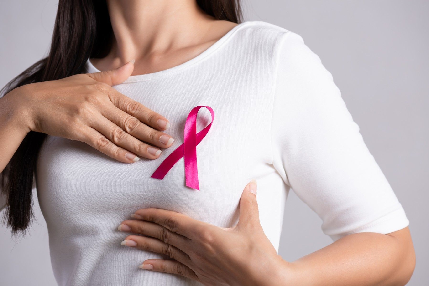 A woman holds her chest showing off a pink Breast Cancer ribbon