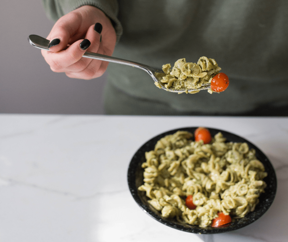 A person holds a fork of pesto pasta