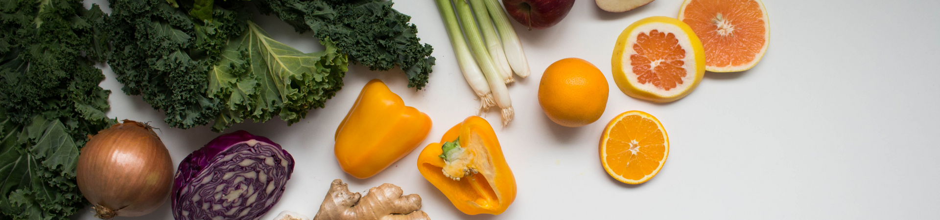 a yellow pepper, green leek, an orange, a grapefruit and ginger sit on a table