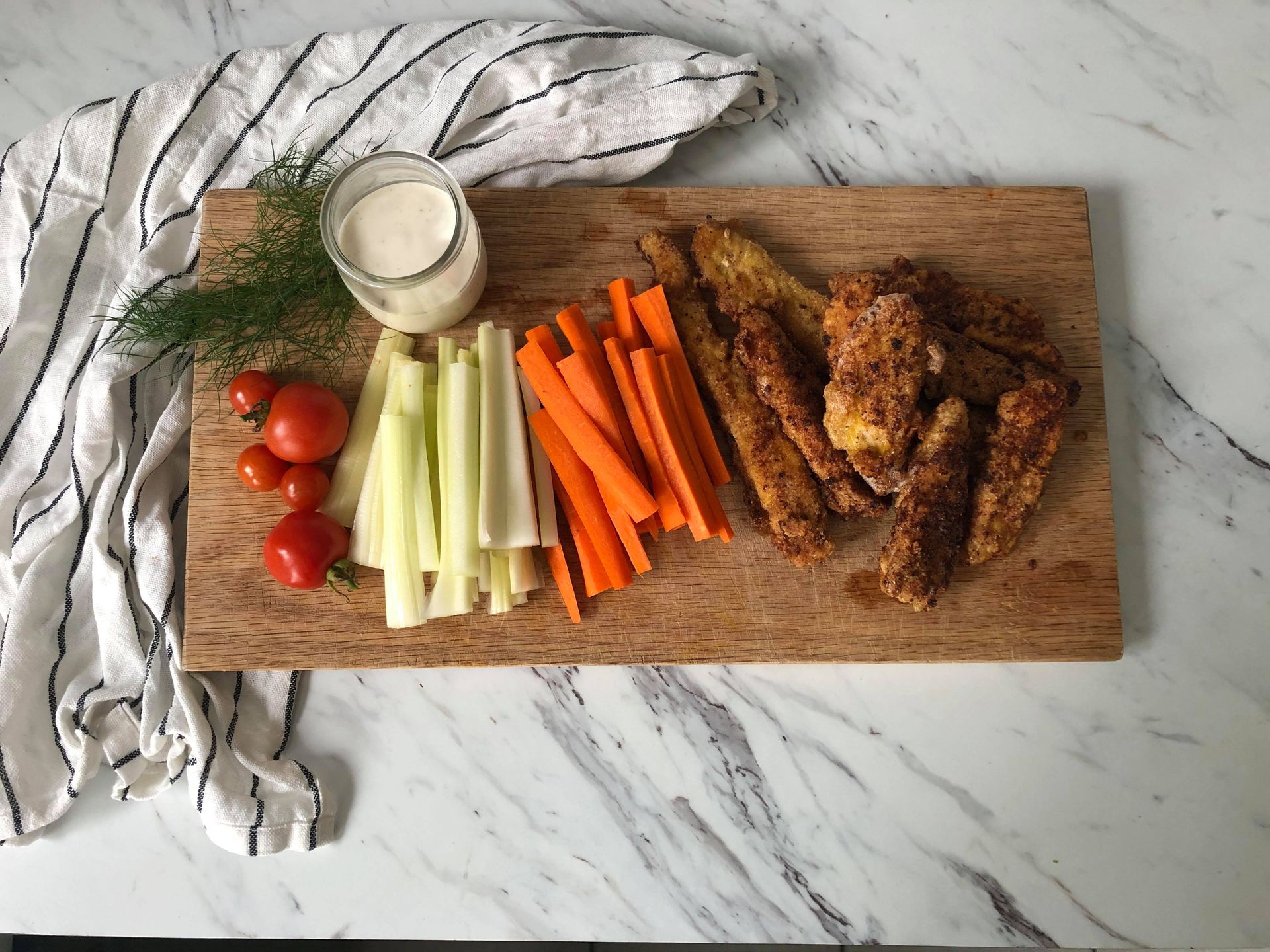 A cutting board with chicken strips, carrots, celery and tomatoes
