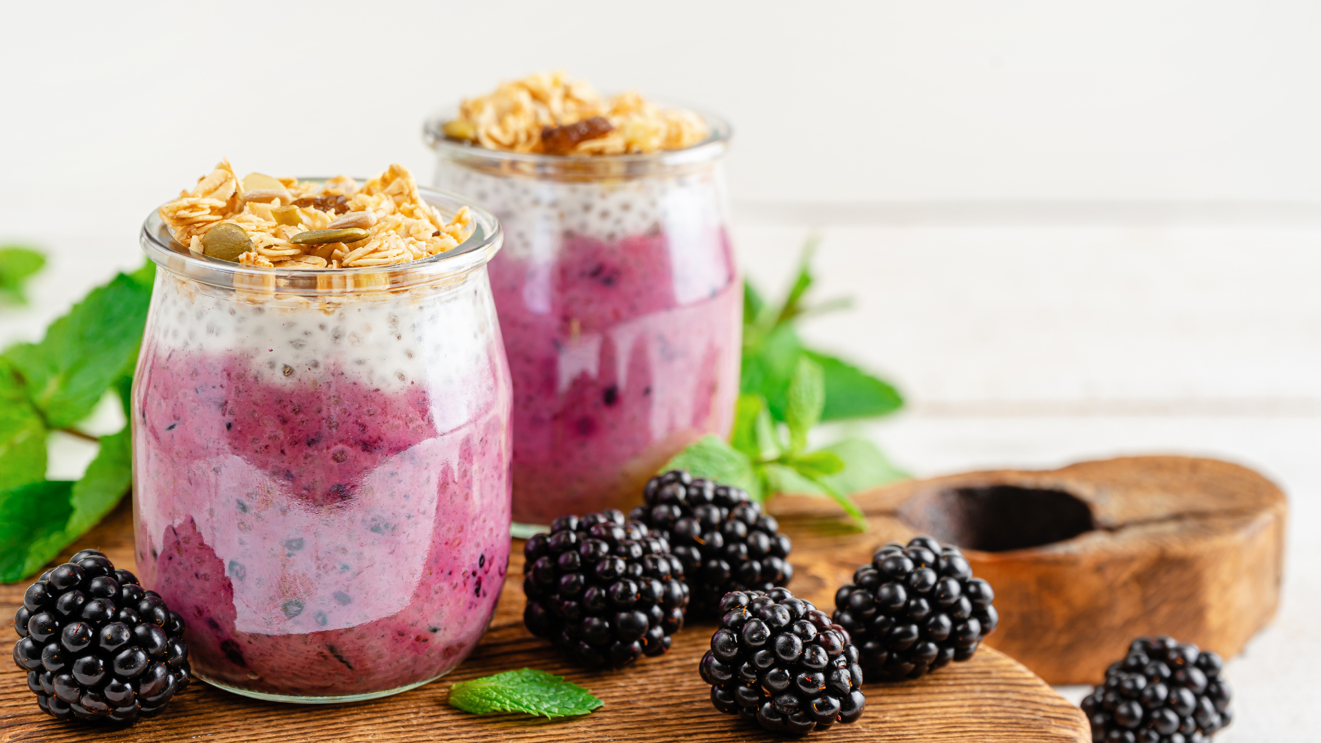 Chia Pudding sits in a glass on a cutting board with blackberries surrounding it on the ground